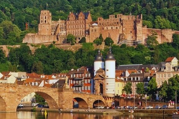 Panoramablick auf das Heidelberger Schloss und die Alte Brücke über den Neckar – historisches Wahrzeichen inmitten grüner Hügellandschaft und urbaner Altstadtarchitektur.