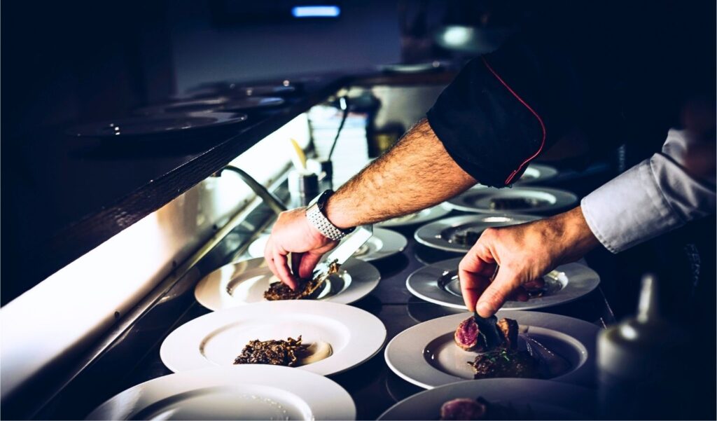 Küchenchef beim Anrichten mehrerer Teller – Gebäudereinigung für Gastronomie mit Fokus auf Hygiene und Küchenlogistik