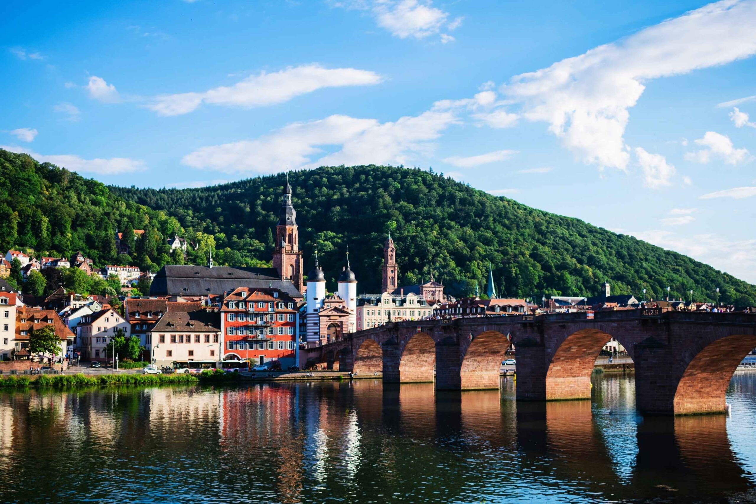 Historische Alte Brücke in Heidelberg über den Neckar mit Blick auf Altstadt und Kirchtürme, in malerischer Flusslandschaft.