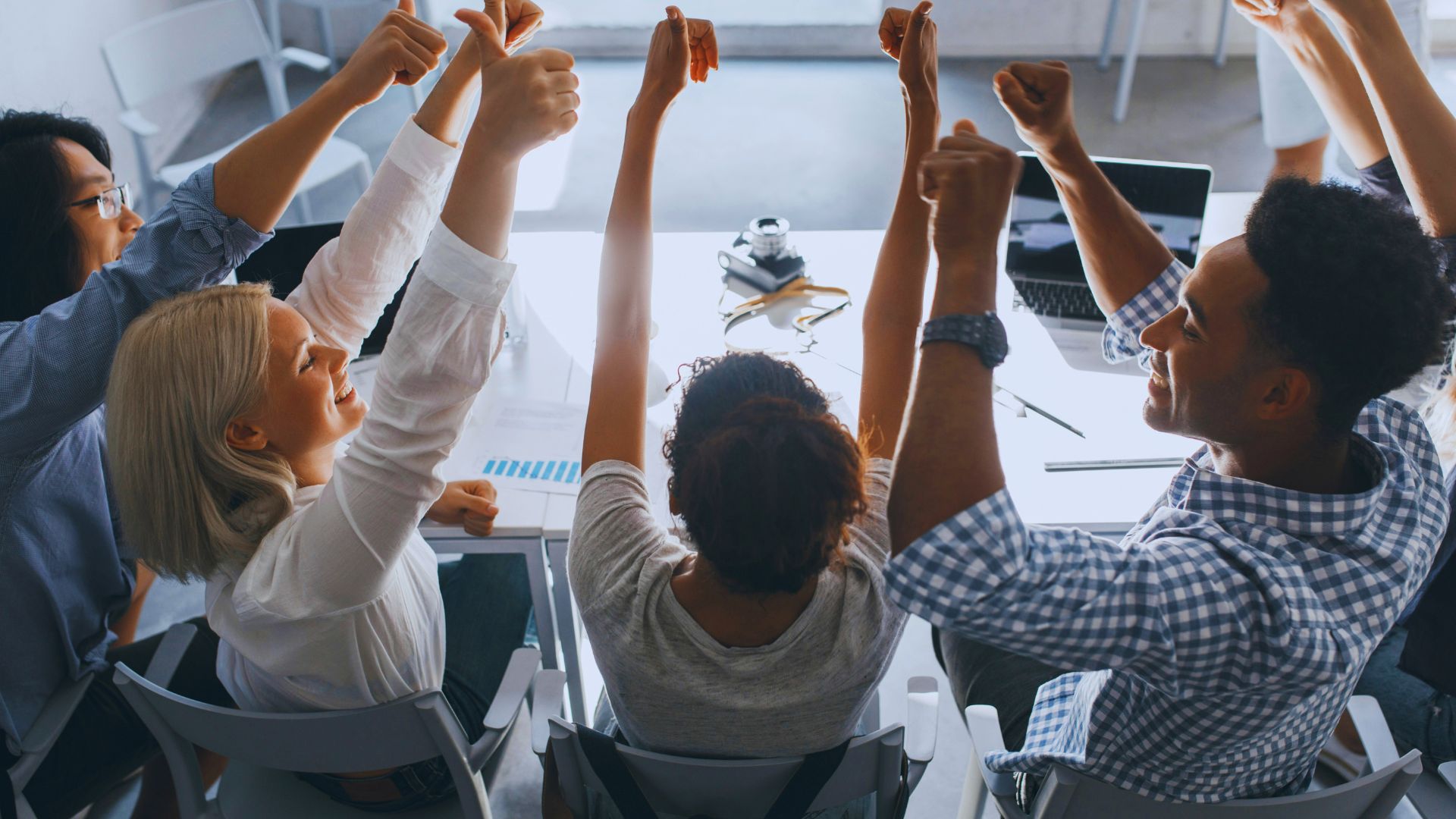 Lacidem Team in einem modernen Büro, das gemeinsam am Tisch sitzt und mit erhobenen Daumen erfolgreiche Zusammenarbeit signalisiert.